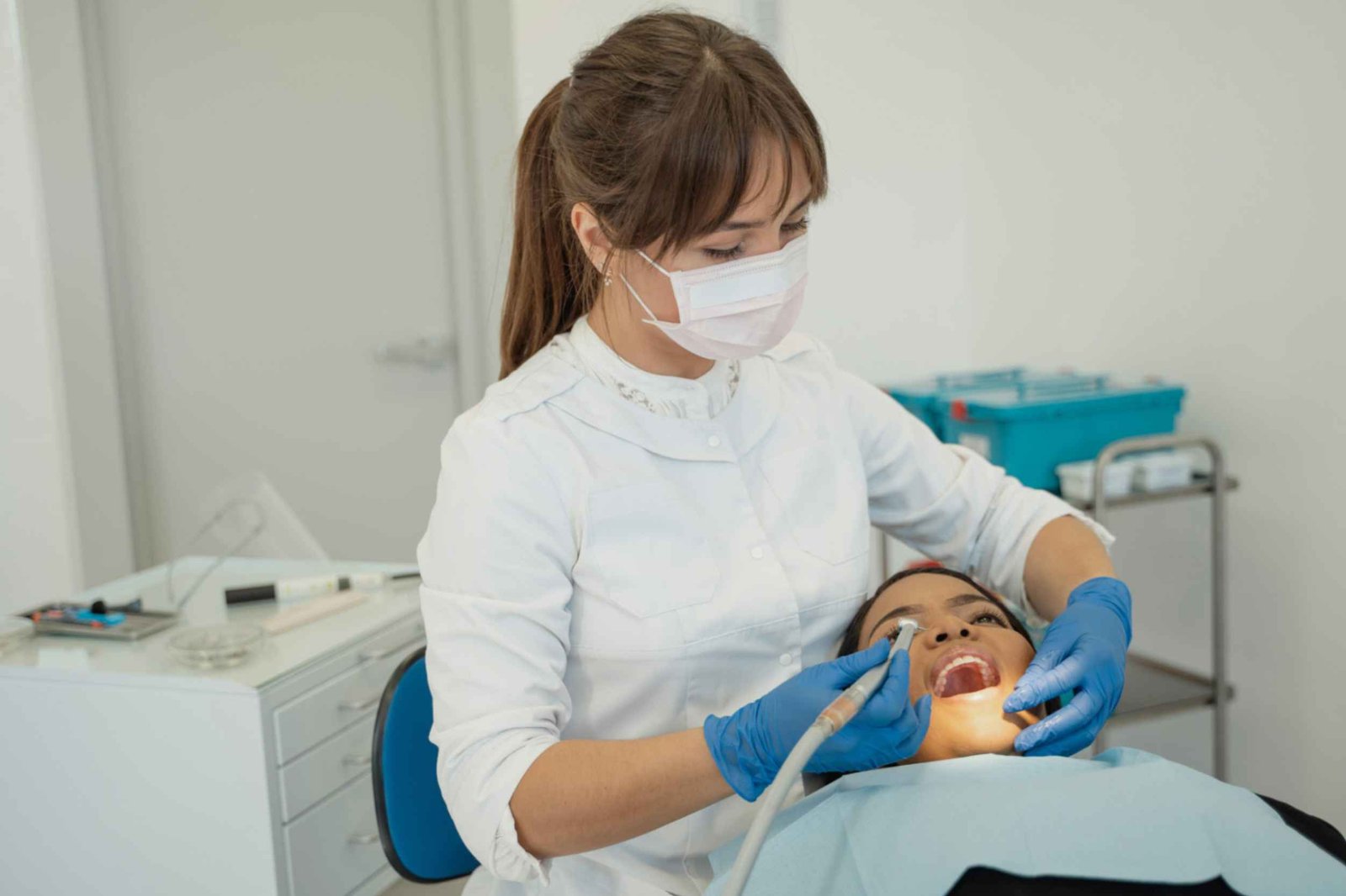 Dental professional in white coat and mask performing oral procedure on patient in dental chair, showcasing commitment to patient care at Peak Performance Health.