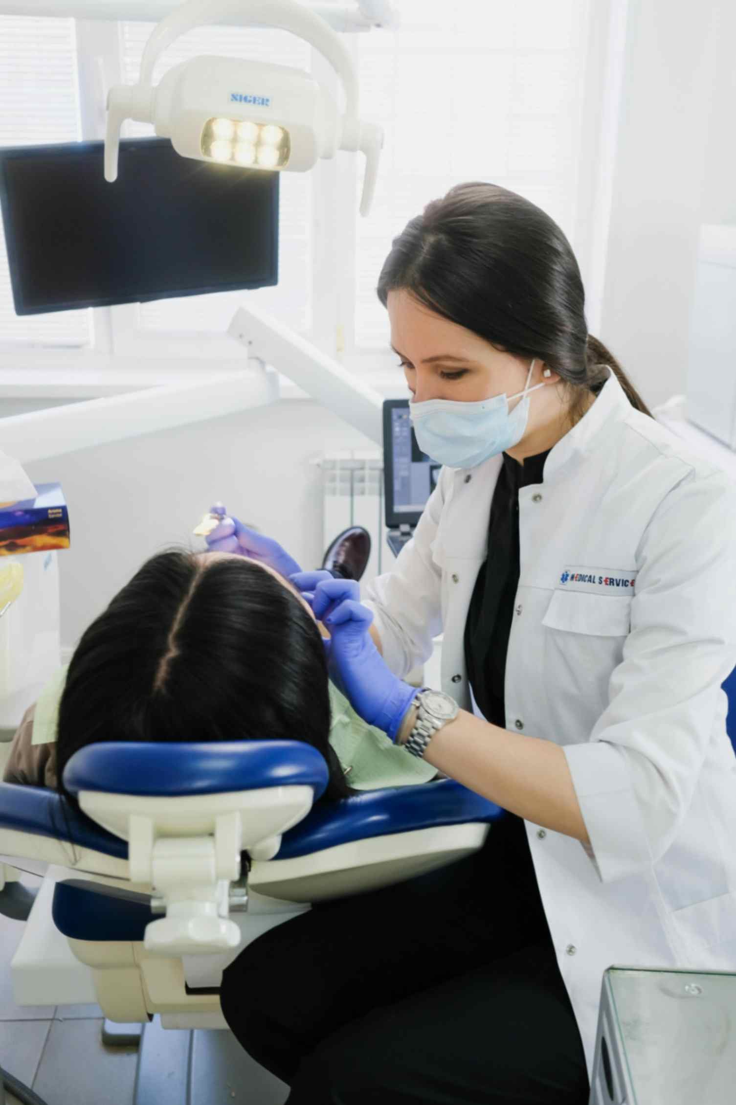Dentist in white coat and gloves performing dental care on patient in dental chair, showcasing professional oral health services at Peak Performance Health.