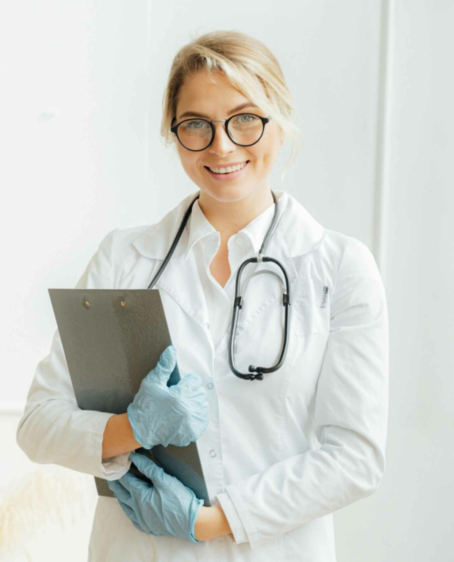 Smiling female dentist in a white coat and stethoscope, holding a clipboard, showcasing professionalism and care in a dental health setting.